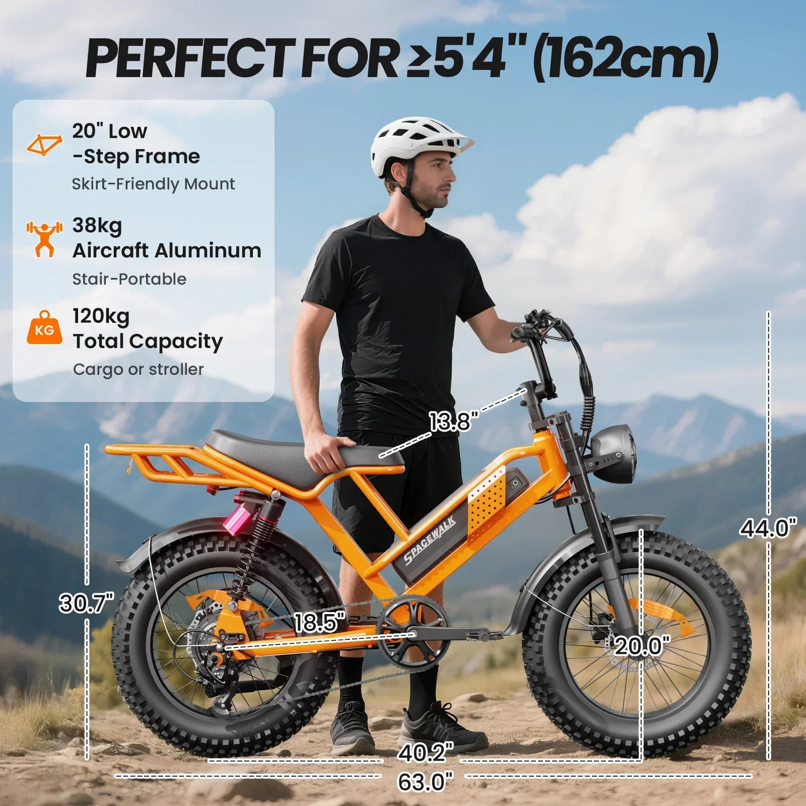 Man with helmet standing beside orange electric mountain bike, showing frame and wheel dimensions, outdoors.
